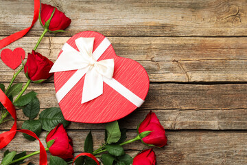 Beautiful heart shaped gift box and roses on wooden background, flat lay with space for text....