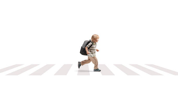 Full length profile shot of a young boy with a backpack running over a pedestrian crossing