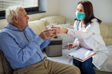Obraz premium Physician providing a glass of water to an elderly patient at home, demonstrating attentive care and support in a warm, comfortable setting.