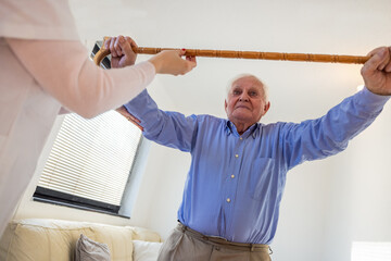 Caregiver assisting elderly man with rehabilitation exercises at home
