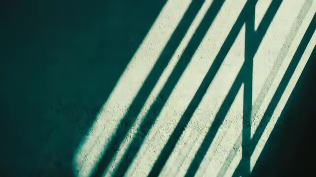 Strong sunlight casting dramatic parallel bar shadows onto a textured wall, forming a striking abstract minimalist composition with contrasting dark and light areas