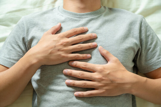 Close up of a man lying down with hands on chest in a grey t shirt. Concept of breath control, relaxation, mindfulness, and calmness in a peaceful environment indoors.