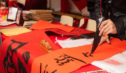 Close up of woman writing Happy New Year with Chinese calligraphy on couplets for celebration. Chinese calligraphy workshop - create traditional festive symbols and Chinese characters