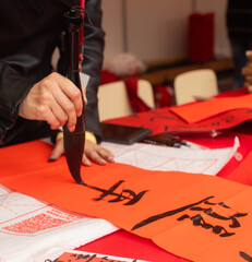 Close up of woman writing Happy New Year with Chinese calligraphy on couplets for celebration. Chinese calligraphy workshop - create traditional festive symbols and Chinese characters