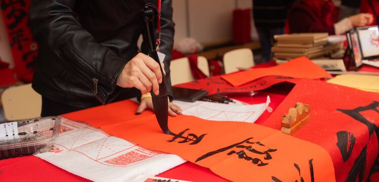 Close up of woman writing Happy New Year with Chinese calligraphy on couplets for celebration. Chinese calligraphy workshop - create traditional festive symbols and Chinese characters