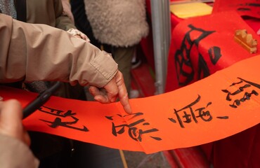 Close up of woman writing Happy New Year with Chinese calligraphy on couplets for celebration. Chinese calligraphy workshop - create traditional festive symbols and Chinese characters