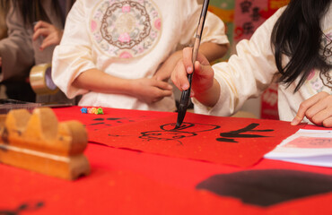 Close up of woman writing Happy New Year with Chinese calligraphy on couplets for celebration. Chinese calligraphy workshop - create traditional festive symbols and Chinese characters