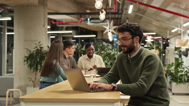Young businessman typing on laptop in modern coworking space