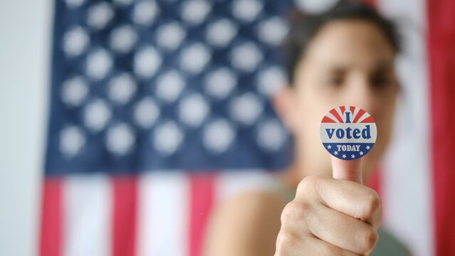 Woman showing i voted today sticker on finger, celebrating civic duty and patriotic participation in usa democratic elections, standing proud against an american flag
