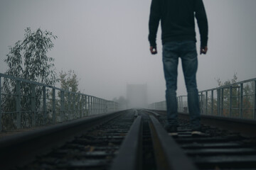 Silhouette of a man walking along a railway in a thick fog, back view
