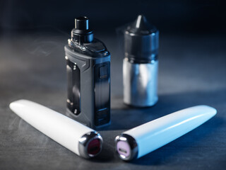 different electronic cigarettes on a dark table and e-cigarette liquid . Modern smoking devices