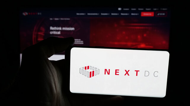 Stuttgart, Germany - 01-21-2026: Person holding mobile phone with logo of Australian data center company NextDC Ltd. on screen in front of web page. Focus on phone display.
