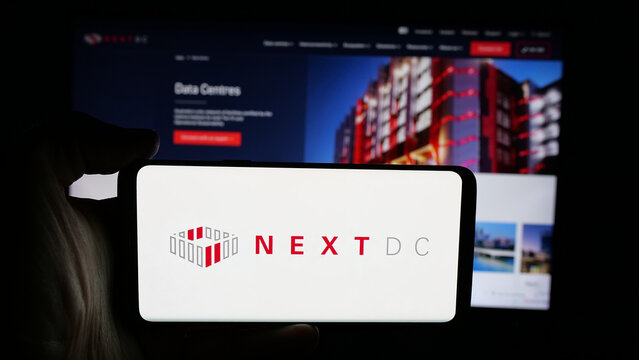 Stuttgart, Germany - 01-21-2026: Person holding cellphone with logo of Australian data center company NextDC Ltd. on screen in front of webpage. Focus on phone display.