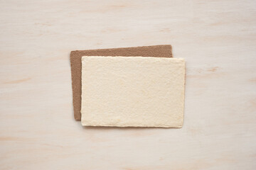 Two sheets of handmade paper on a wooden background