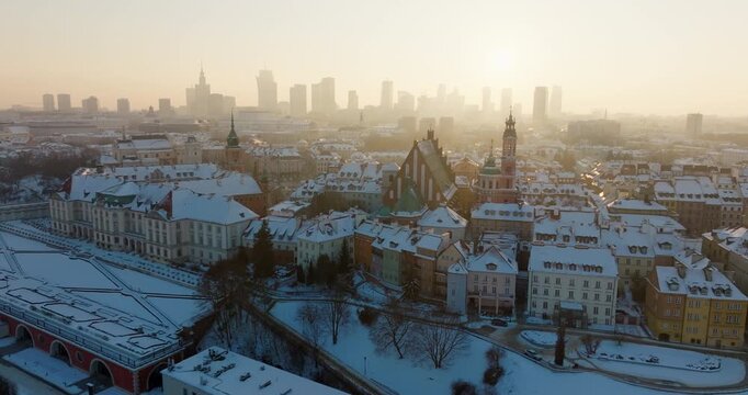 Cinematic drone view of Warsaw, Poland in winter. Establishing zoom in aerial shot of snowy Old Town landmarks. Royal Castle and Cathedral with the modern downtown business skyline in sunny haze