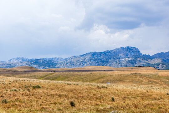 Vast golden plains extend toward rugged mountains beneath a moody, overcast sky