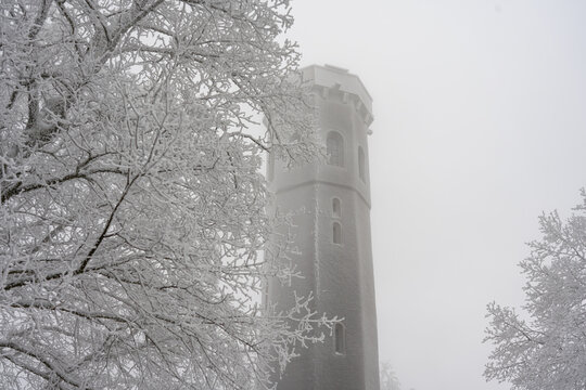 Horizontal view of a stone tower surrounded by white frosted trees in dense fog.