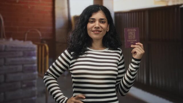 Woman holds czech passport up in building interior near brick wall with hand on hip; confidence travel identity.