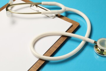 Stethoscope and clipboard on light blue background, closeup