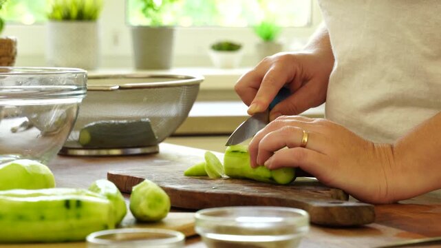 Woman cutting fresh cucumber for salad
