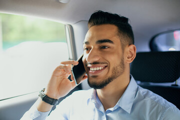 Happy middle-eastern young man manager talking to business partner on cellphone while going to...