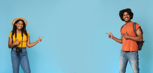 Cheerful black man and woman with backpacks and camera travellers showing empty space for...