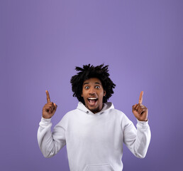 Cool black teenager pointing upwards with both hands on violet studio background, space for your ad...