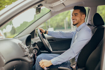 Cheerful arab businessman driving nice car, young middle-eastern manager or entrepreneur goign to...