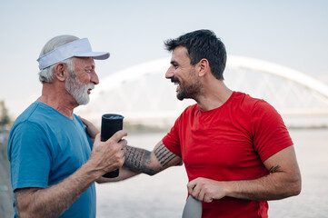 Senior man and personal trainer talking and smiling after workout by the river