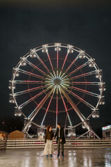Couple ice skating holding hands in front of ferris wheel
