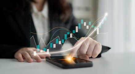 A business professional uses a smartphone to analyze stock market trends, featuring digital graphs...