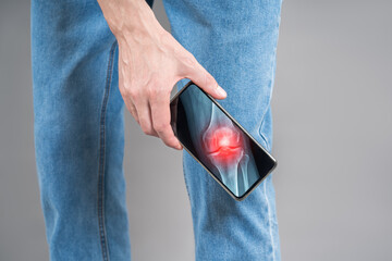 Man holding smartphone with digital x-ray of knee joint showing pain and inflammation, telemedicine...
