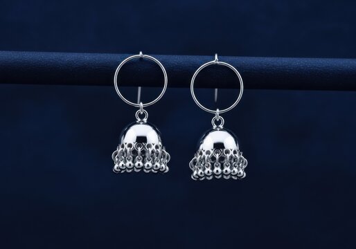 A pair of silver jhumka earrings on a dark blue background with hoop and bell shaped danglers