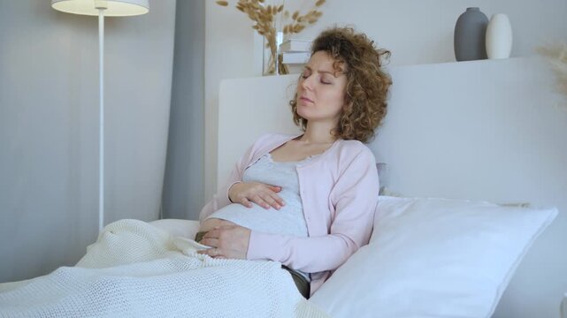 Expectant mother lying in bed and stroking her belly while experiencing painful braxton hicks contractions, feeling discomfort and anxiety during the third trimester of her pregnancy