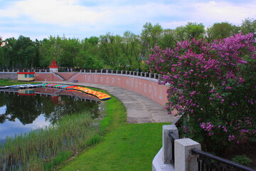 Scenic city park with a brick walking path, lush green trees, and a sunset reflection on the river