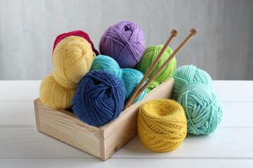 Knitting yarns and needles in box on white wooden table, closeup