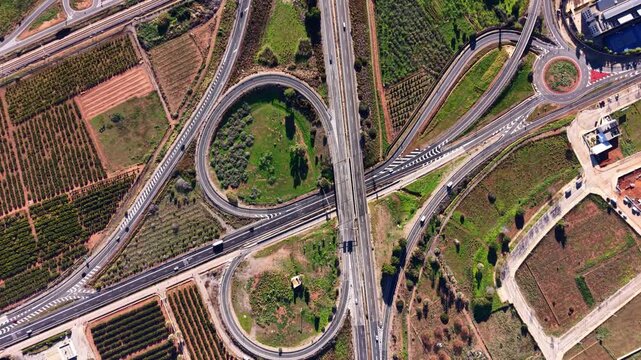 Vertical aerial view of a cloverleaf highway interchange in Spain Valencia region, showing curved ramps, multilane roads, traffic flow and surrounding agricultural landscape.