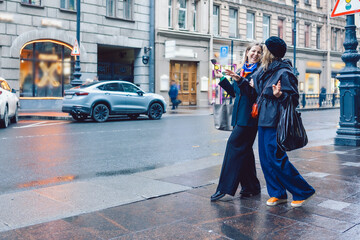 Two female friends are walking through city streets and looking at shop windows 