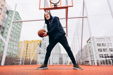 Stylish senior basketball player holding ball standing on playground with basketball hoop outdoors © Maria Vitkovska