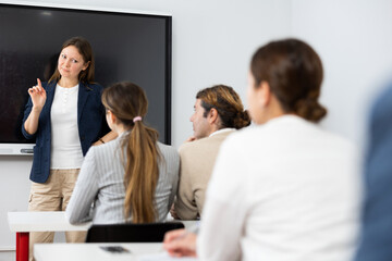 Fototapeta premium Female business coach gesturing with hand while standing against group of people sitting at chairs in front of her