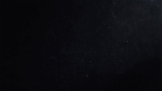 Close-up of micro dust particles floating slowly in dark background with ethereal light glimmers, creating atmospheric haze overlay