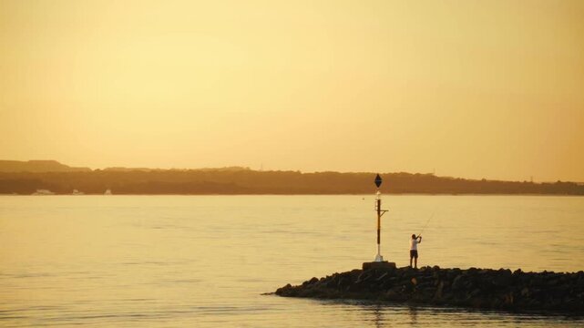 Fisherman on Rocky Breakwater Buoy Pole at Ramsgate Beach Sydney Golden Hour Sunset with Calm Bay Waters