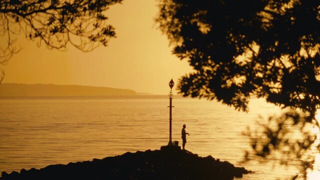 Silhouette of Fisherman on Breakwater Lamp Post at Ramsgate Beach Golden hour with Tree Branches Foreground