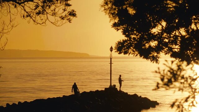 Silhouettes of Two Fishermen on Ramsgate Beach Breakwater Lamp Post at Sunset with Branch Foreground Framing Calm Sea