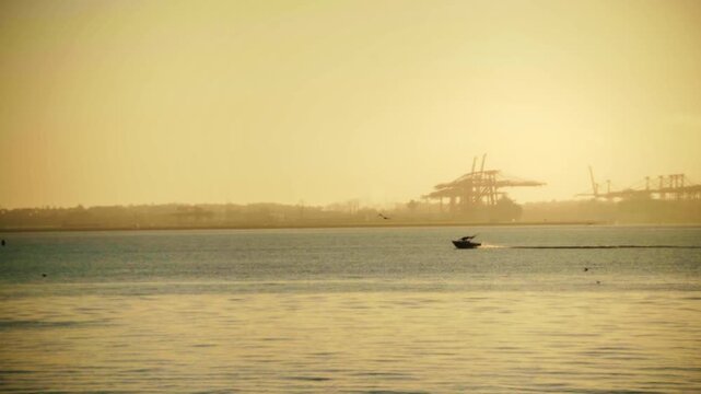 Motorboat Cruising Across Ramsgate Beach Bayside at Golden Sunrise with Industrial Port Silhouette in Distance.