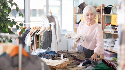Mature woman spend time in shop and chooses sweater. Changing wardrobe, shaping style of clothing,...