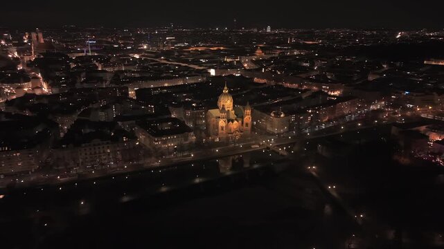 Munich night skyline via drone. The view spans from St. Lukas Church by river to the distant, brightly lit towers of Frauenkirche and the spires of the historic city center. Luftaufnahme Muenchen