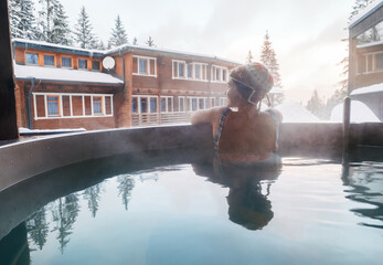 Young woman relaxing in Hot water jacuzzi outdoor bathtub in winter forest wellness hotel and...