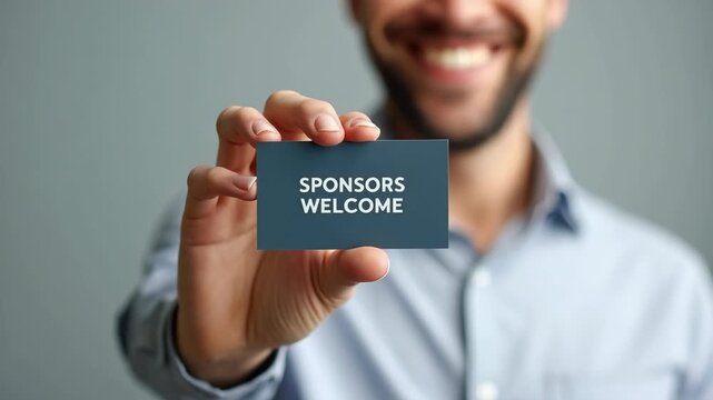 Man showing business card with text Sponsors Welcome on grey background, closeup.