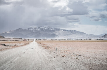 The asphalt road of the Pamir Highway stretches into the distance against a backdrop of snow-capped rocky mountain ranges, a panoramic view in the Tien Shan Mountains of Tajikistan